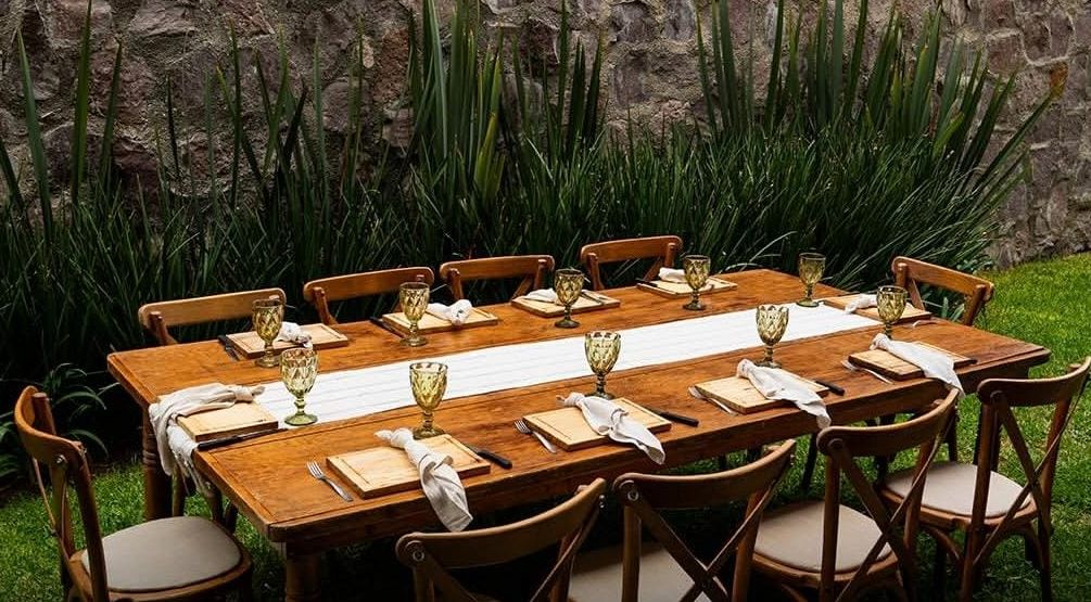Mesa de madera montada en un jardín con copas, servilletas y camino de mesa