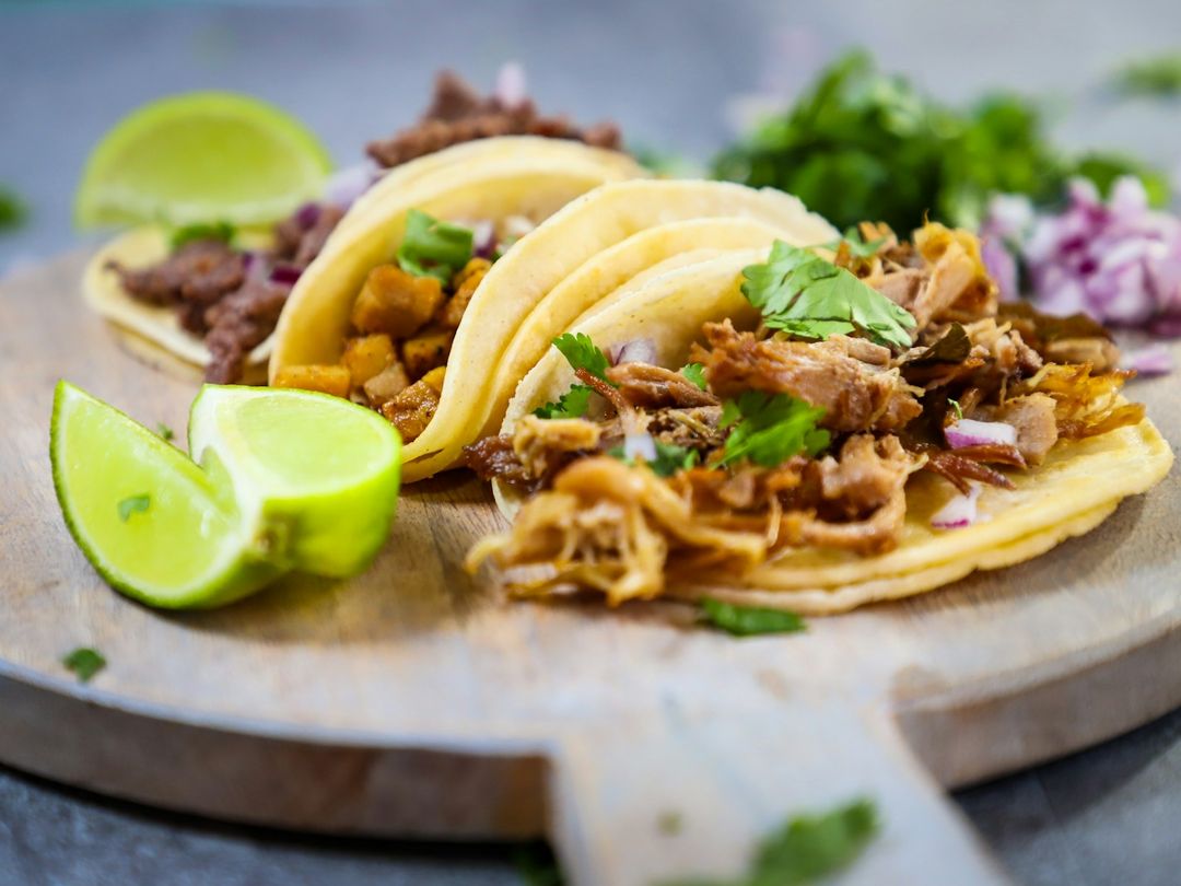 Tacos de pastor y bistec sobre una tabla de madera con limón